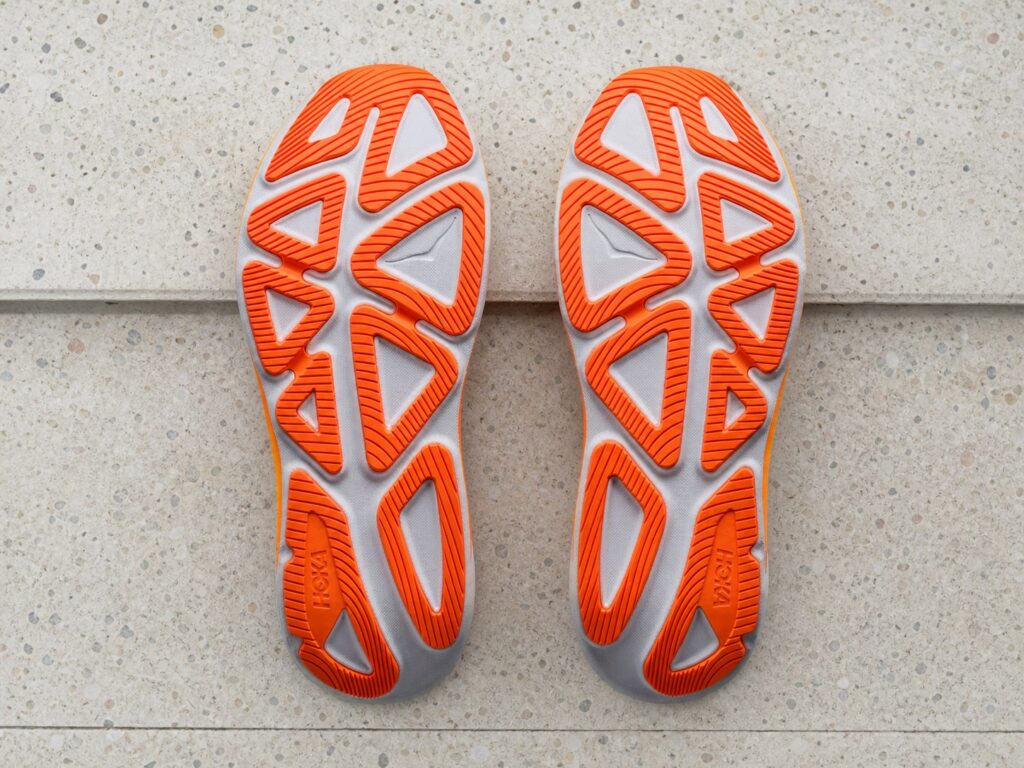 Semelles extérieures orange des HOKA Clifton Pro sur du terrazzo clair
