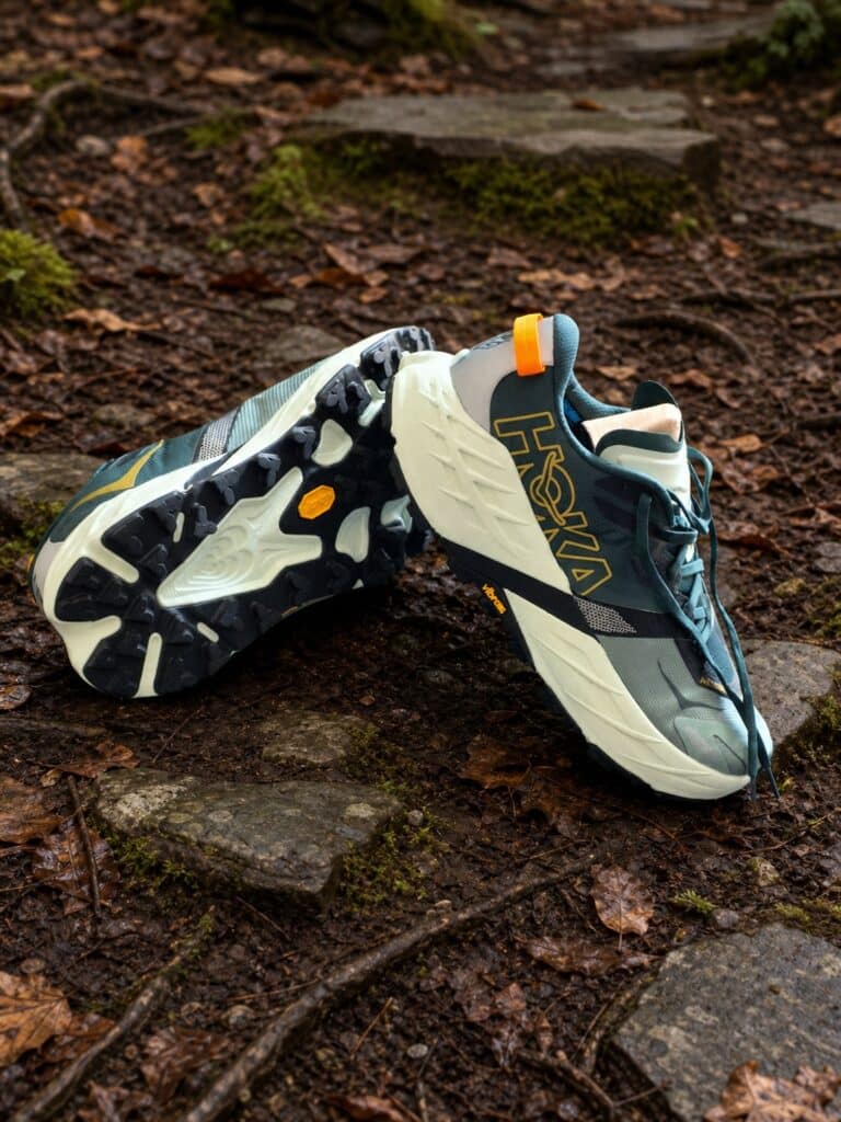 HOKA Speedgoat 7 grises sur un sentier forestier humide