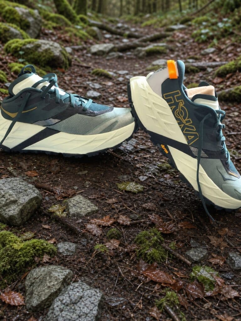 Profils des HOKA Speedgoat 7 grises sur un chemin forestier humide