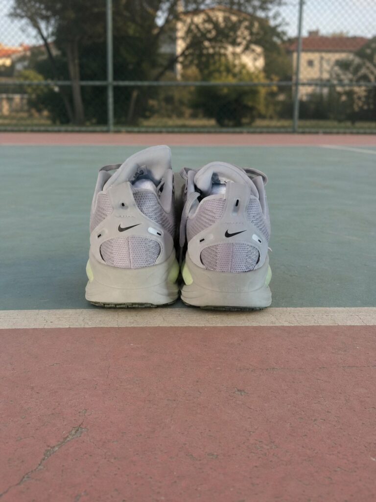 Vue arrière des Nike Vomero 18 homme sur un terrain sportif vert d’eau