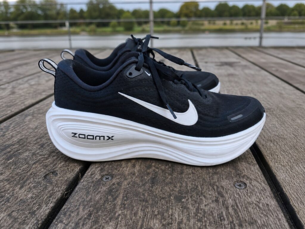 Nike Vomero Plus homme noire et blanche sur une passerelle en bois au bord de l’eau