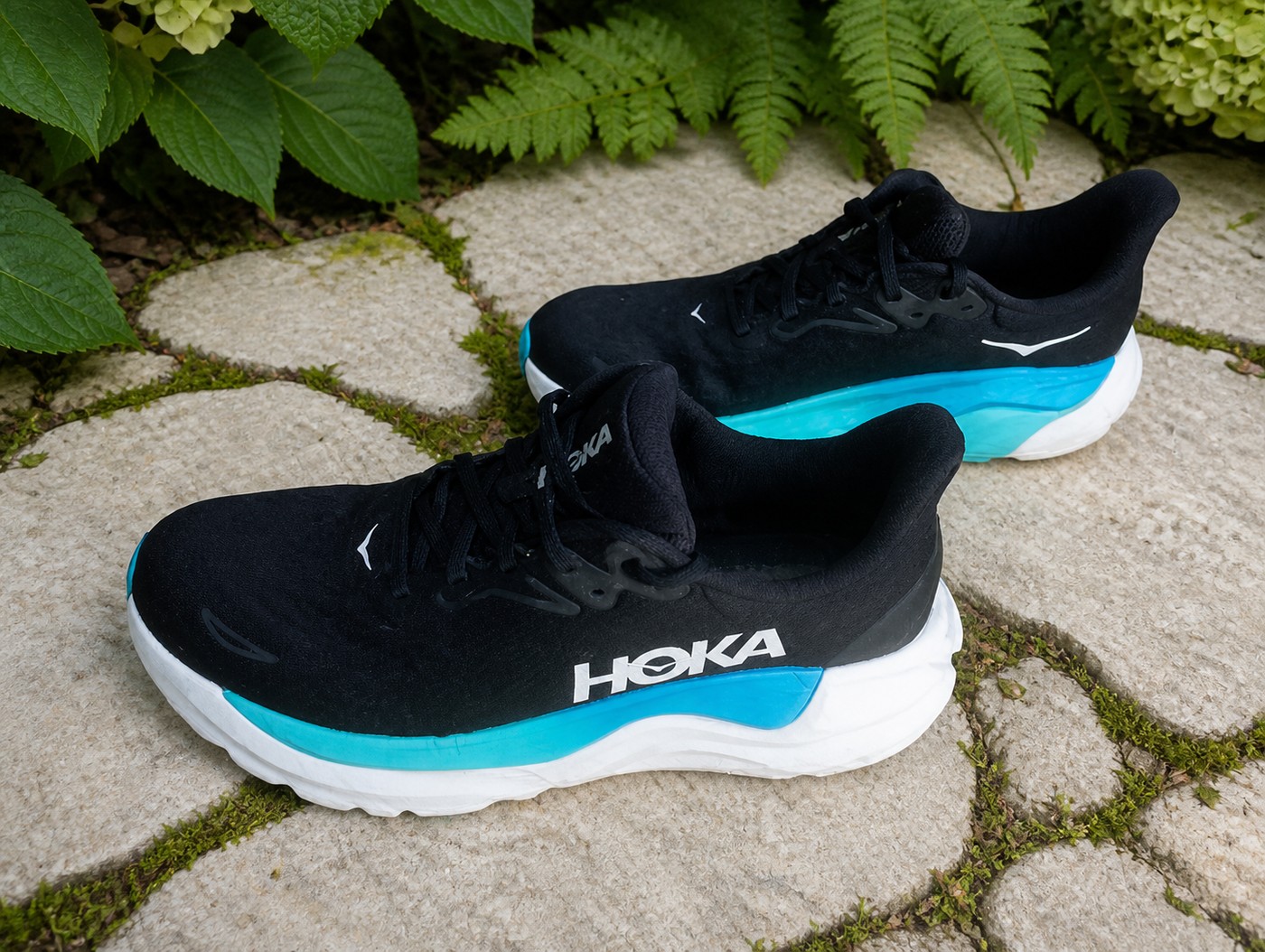 Vue du dessus des HOKA Arahi 8 noires et turquoise dans un jardin